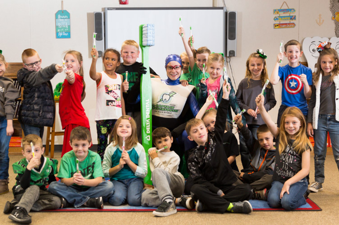 Captain Supertooth in a superhero costume with a group of kids in a classroom