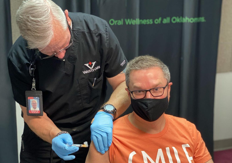 Man administering a shot to another man in a face mask