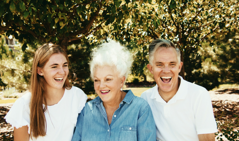 Family laughing outdoors: young woman, older woman, and man.